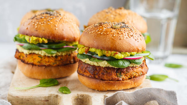 Healthy baked sweet potato burger with whole grain bun, guacamole, vegan mayonnaise and vegetables on a wooden board. Vegetarian food concept, light background. 