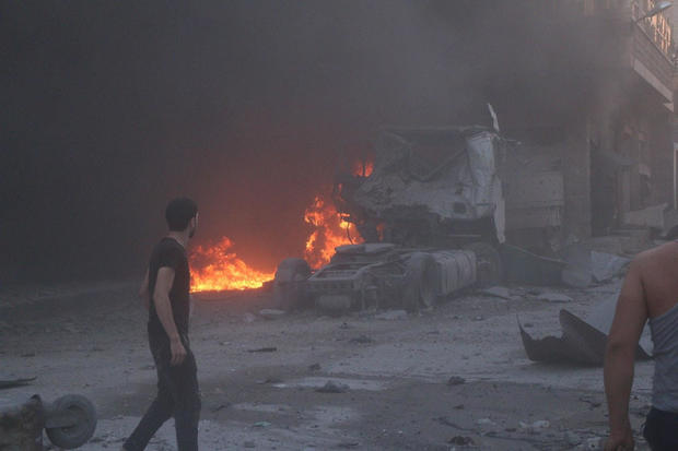 People walk next to fire, debris and a damaged truck after a deadly airstrike, said to be in Maarat al-Numan 