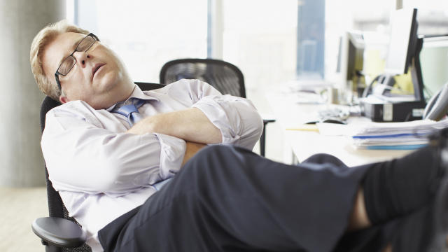 Businessman sleeping with feet up at desk 