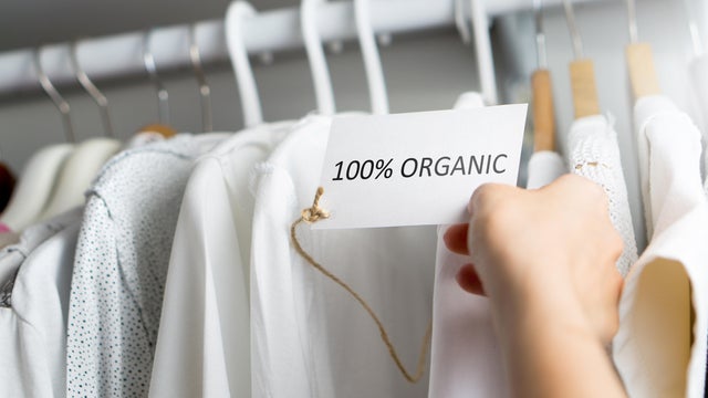 T-shirt made of 100% and hundred percent organic materials. Customer with responsible and nature and eco friendly values looking for clothes in store or shop. Holding label and price tag with text. 