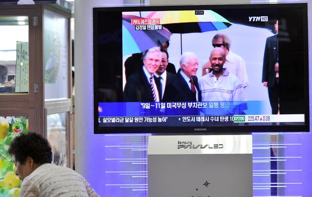 A woman walks past a TV screen reporting 