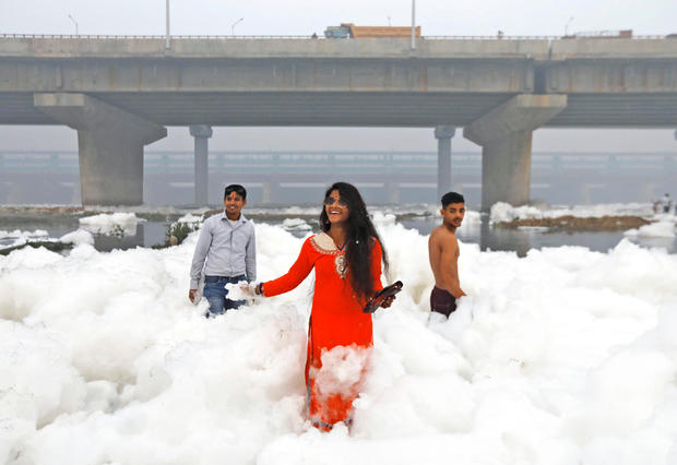 People pose for pictures as they stand amidst the foam covering the polluted Yamuna river on a smoggy morning in New Delhi 