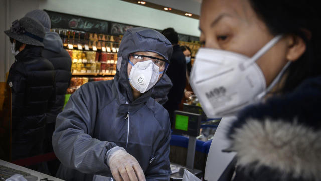 A Chinese worker wears a protective suit and mask as she scans groceries for a customer at a supermarket on February 11, 2020, in Beijing, China. 