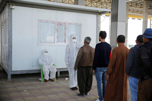 Members of the medical team check the temperature of Iraqi men, following the coronavirus outbreak, at the entrance checkpoint of South Mosul 