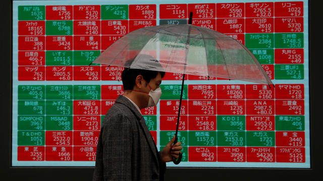 A visitor wearing protective face mask, following an outbreak of the coronavirus, walks past in front of a stock quotation board outside a brokerage in Tokyo 