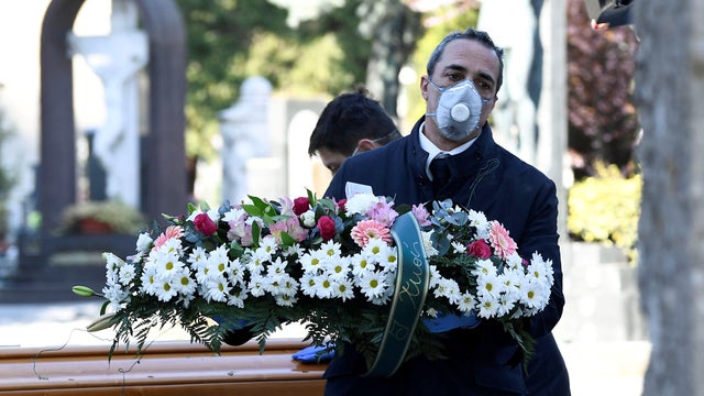 Cemetery workers and funeral agency workers in protective masks transport the coffin of a person who died from the coronavirus disease COVID-19 into a cemetery in Bergamo, Italy, March 16, 2020. 