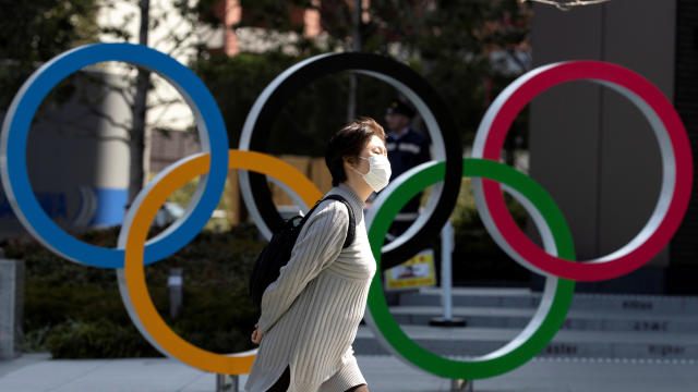 A woman wearing a protective face mask amid an outbreak of the coronavirus disease COVID-19 walks past the Olympic rings in front of the Japan Olympics Museum in Tokyo, Japan, March 13, 2020. 