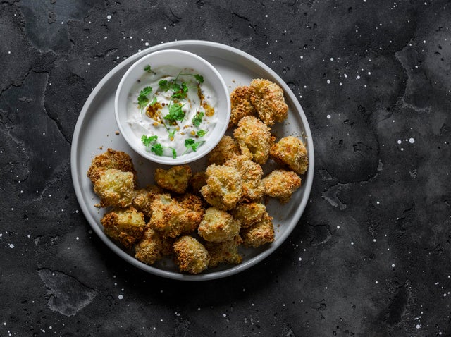 Baked crispy parmesan bread crumbs cauliflower bites with yogurt sauce on dark background, top view 