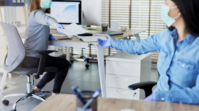 Two people in office passing documents with keeping a distance 