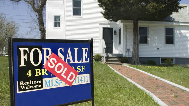 'For Sale' sign on lawn in front of house 