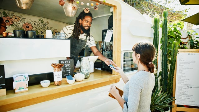Smiling food truck owner taking credit card for payment from customer 