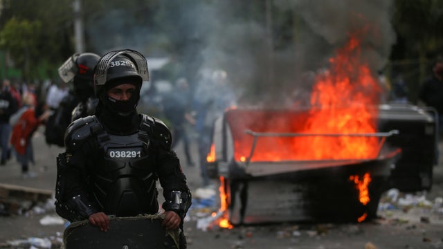 Riot police stand next to a burning garbage container during clashes with protesters after a man, who was detained for violating social distancing rules, died from being repeatedly shocked with a stun gun by officers, according to authorities, in Bogota 