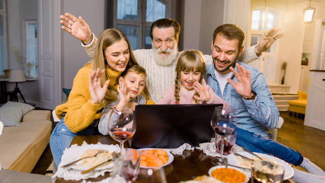 Beautiful family, sitting at the table with dinner meal, smiling, happy and using laptop. Family making videocall using laptop celebrating at home 