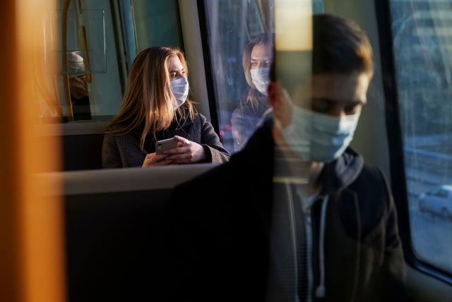 young woman sitting in train wearing protective mask, using smartphone 