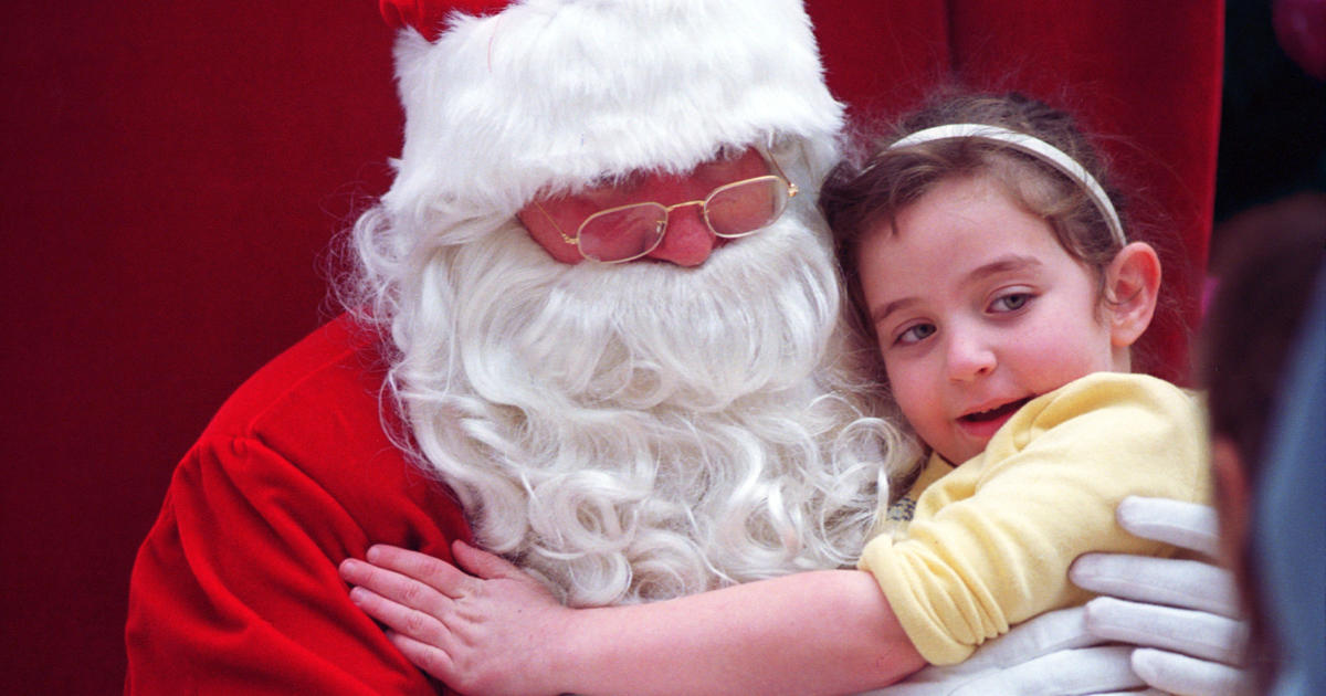 A performer dressed as Santa Claus sits behind a Plexiglas barrier