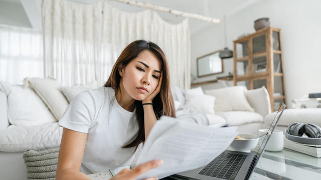 Stressed and worried young Asian woman working from home, handling paperworks and going through her financials 