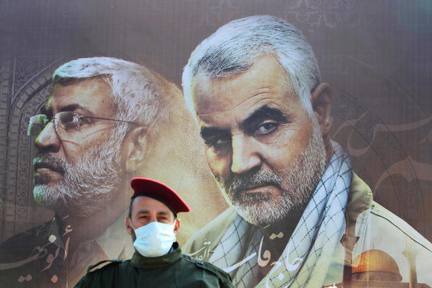 A member of Lebanon's Hezbollah stands in front of a picture depicting senior Iranian military commander General Qassem Soleimani and Iraqi militia commander Abu Mahdi al-Muhandis, during a ceremony marking the first anniversary of their killing, in Khiam 