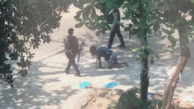 Police officer carrying a rifle forces a man to crawl on all fours in Yangon 