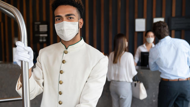 Happy bellboy working at a hotel and wearing a facemask to avoid COVID-19 