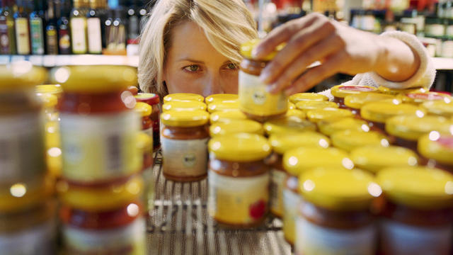 Young woman selecting jar from shelf in shop (focus on woman's face) 