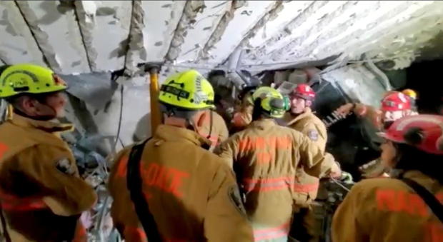 Fire crew members work at the basement parking garage of partially collapsed residential building in Surfside, Florida 