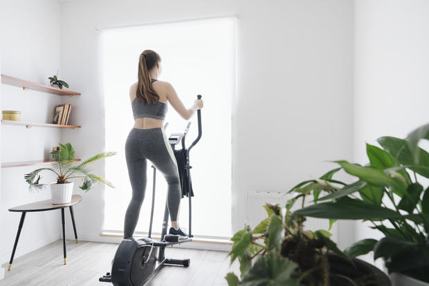 Woman performing workout on elliptical trainer at home 