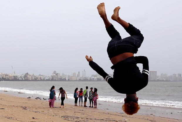 FILE PHOTO: Beachgoers stroll as a boy practices somersaulting on a beach in Mumbai 