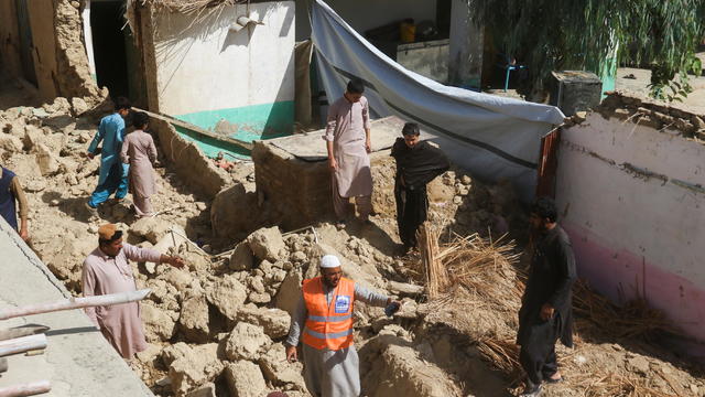 Rescue worker and residents stand amid the rubble of a damaged house following an earthquake in Harnai 