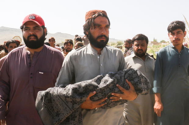 A man carries the body of a child, who died following an earthquake, during a funeral in Harnai 
