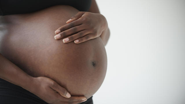 Midsection of pregnant Black woman holding belly 
