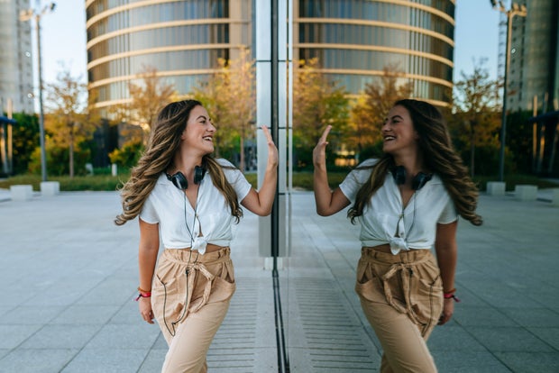 self love  Young smilimg woman reflected in glass clashing her hand with herself 