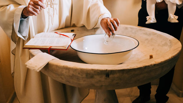 Priest throws the sacred water into the baptismal font during a baby's baptism 