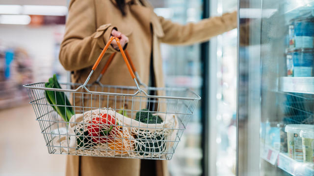 Cropped shot of woman carrying shopping basket and shopping groceries in supermarket 