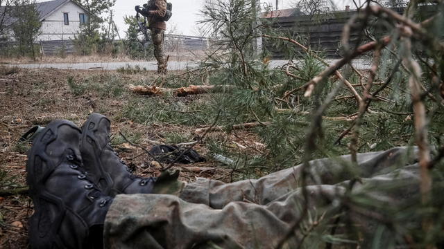 A Ukrainian service member stands near a body of a Russian soldier on the front line near Kyiv 