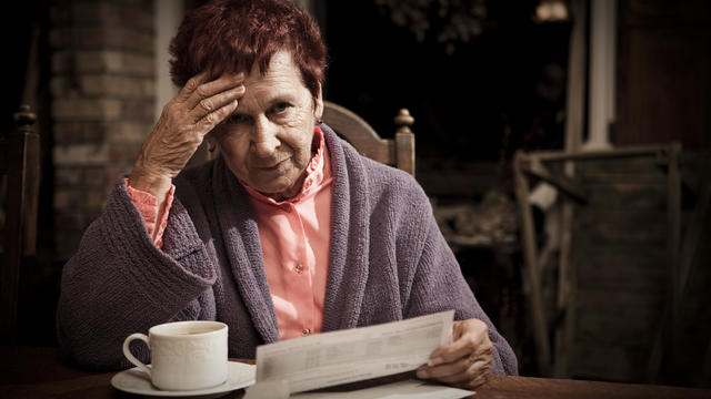An elderly lady sat looking stressed reading bills 