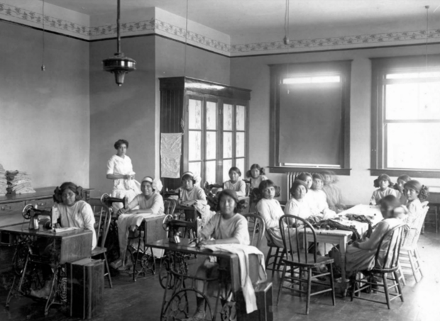 Young female students seated with sewing machines in classroom at the Phoenix Indian Industrial School. 