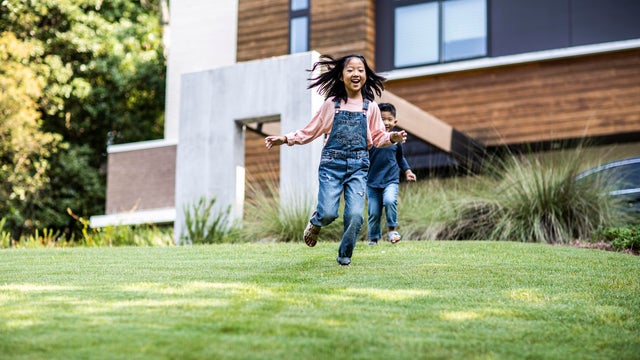 Brother and sister running in front yard of modern home 