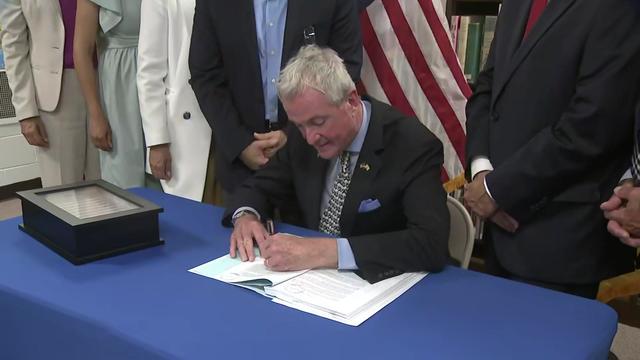 New Jersey Gov. Phil Murphy sits at a table and signs the state budget 