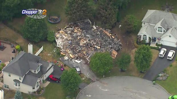 An aerial view shows a large pile of rubble from a burned-down house between two undamaged homes 