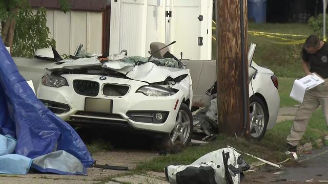 A badly damaged white BMW sedan sits on a sidewalk next to a telephone pole. 