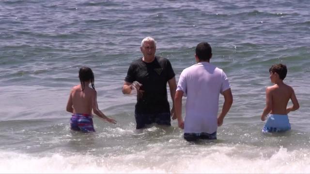 Nassau County Executive Bruce Blakeman stands in the ocean with water about up to his waist along with two children and an adult. 