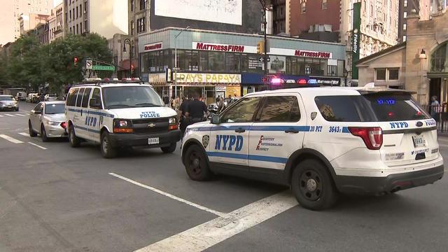 Two NYPD vehicles sit parked on the street outside the entrance of a subway station. 