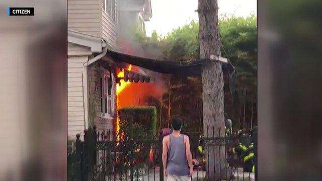 Large flames can be seen on the side of a house. 