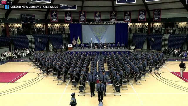 163 New Jersey state troopers stand in a triangular formation on a basketball court at their graduation ceremony. 