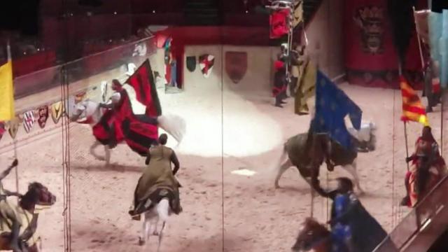 Performers dressed in medieval costumes ride horses in a sandy arena at Medieval Times. 