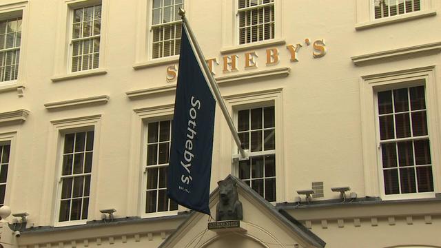 The exterior of a building with a sign reading "Sotheby's" and a Sotheby's flag. 