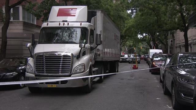 A tractor trailer sits parked on a street behind crime scene tape. 