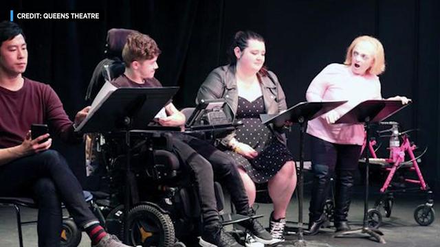 Four acting students sit on a stand, looking at pages on music stands in front of them. One individual is in a wheelchair. Another individual has a walker. 