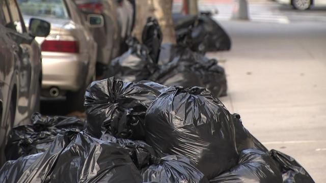 Trash bags sit piled on the curb on a New York City sidewalk. 