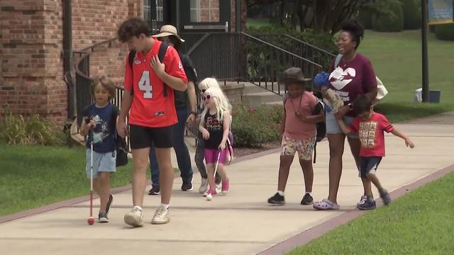 Three young adults walk with five young children, some of whom are carrying canes. 